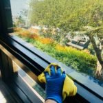 A hand with a yellow rag house cleaning a window.